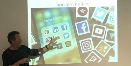 En mand står og peger på en powerpoint med ikoner fra sociale medier som facebook,instagram, twitter